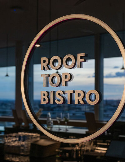 Das B1 Rooftop Bistro Logo. Die Skyline von Basel spiegelt sich dunklen hochglanzmaterial der Wände.